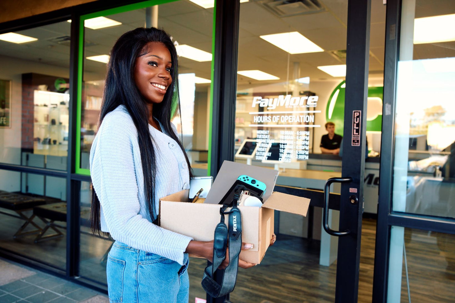 woman walking into paymore with a box of electronics